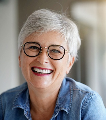 Mature woman smiling in denim shirt and black-framed glasses