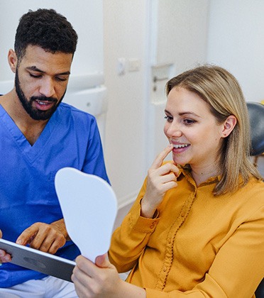 Patient looking at smile in mirror with dental assistant