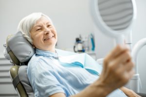 an older woman smiling in the dentist’s chair after receiving dental implants